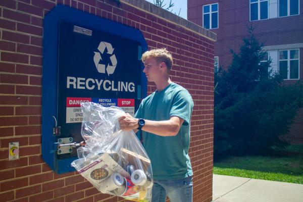 Henry tosses a bag of recyclables into the recycling compactor.