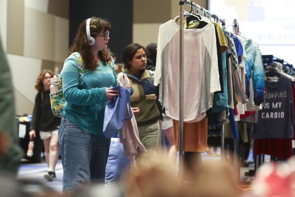 Students stand in front of clothing rack holding tote bags filled with clothes