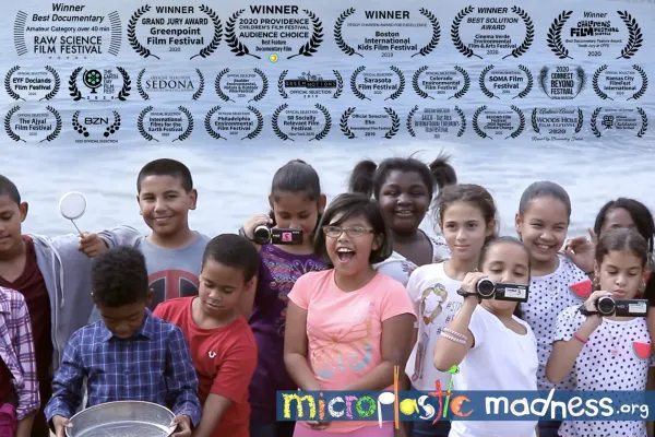 fifth graders standing in front of body of water holding cameras film accolades on top half of image