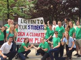 A collection of students wearing green, holding up a sign that says listen to your students, sign a climate action plan.