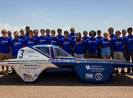 Around 20 people stand in front of the UK Solar powered car. 