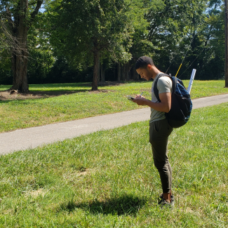 A man standing in a field with a pencil and notebook, writing something down