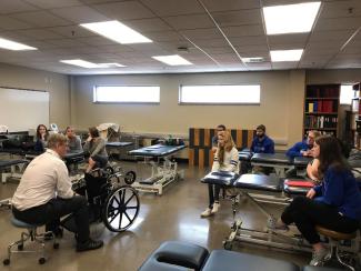 A collection of students are listening to a teacher in the middle of a classroom dedicated to physical education.