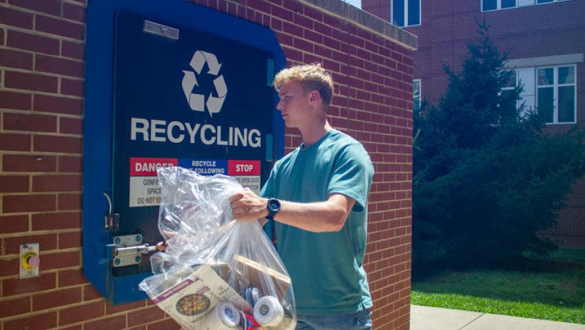 Henry tosses a bag of recyclables into the recycling compactor.