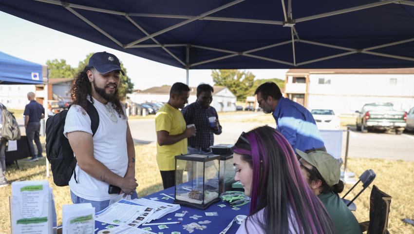 student speaks with vendors at sustainability festival the table has terrariums and stickers on it