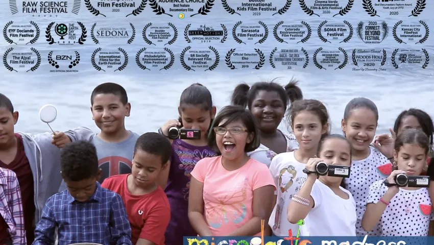 fifth graders standing in front of body of water holding cameras film accolades on top half of image
