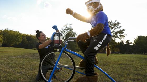 Man poses next to Wildcat Mascot riding bike